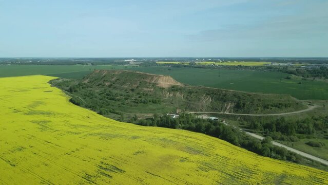 A field of blooming yellow rapeseed. At the edge of the field is a mothballed city dump. Aerial photography.