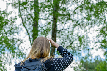 Dziewczyna wpatrująca się w korony drzew liściastych w poszukiwaniu małych ptaków 