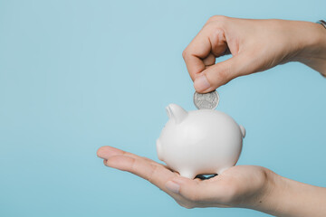 Hand saving a coin into piggy bank  on blue background for investment, business, finance and saving...