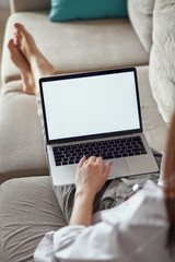 Fototapeta na wymiar Mockup white screen laptop woman using computer lying on sofa at home, back view, focus on screen