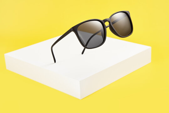 Sunglasses float in air above white square podium.