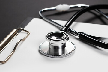 A clipboard and stethoscope with white paper on it, set against a dark background