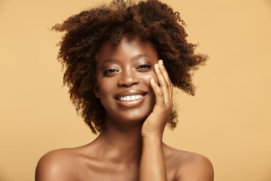 Smiling dark skinned girl touches healthy face skin.