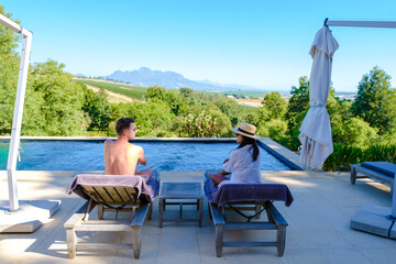 Couple of men and women relaxing at a swimming pool with a view over a Vineyard landscape at sunset...