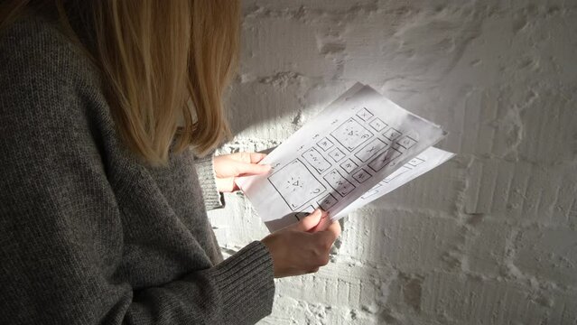 Woman designer looks through website design prototypes and wireframe. UI/UX designer at work. Create sketch for future design project. Web studio workspace