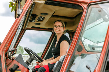 Female farmer concept: Portrait of a young blonde woman beneath a tractor in spring outdoors