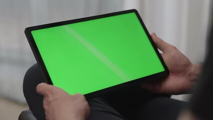 Man sitting indoors on a chair with tablet pc with green screen