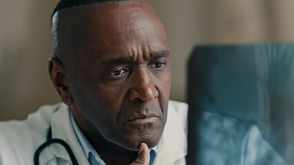 African male medic expert radiologist osteopath surgeon orthopedist ethnic man doctor look at x-ray image roentgen of MRI tomography analyzing trauma broken skeleton bones surgery medicine at hospital