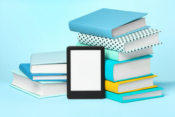 Modern e-book reader and stacks of hard cover books on light blue background