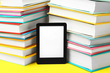 Modern e-book reader and stacks of hard cover books on yellow background, closeup