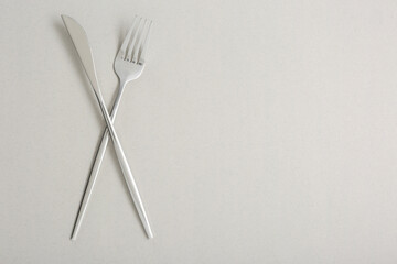 Shiny fork and knife on light grey background, flat lay. Space for text