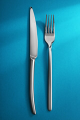 Shiny fork and knife on light blue background, flat lay