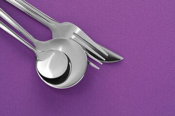 Fork, knife and spoons on purple background, flat lay with space for text. Stylish cutlery set