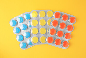 Blisters with cough drops on yellow background, flat lay