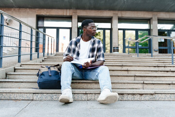 Pensive African student reading book sitting on University Campus staircase