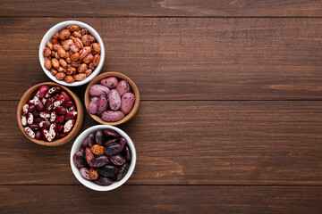 Different kinds of dry kidney beans on wooden table, flat lay. Space for text