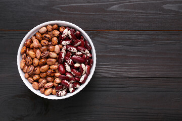 Different kinds of dry kidney beans in bowl on wooden table, top view. Space for text