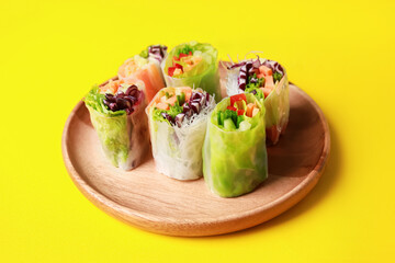Different delicious spring rolls wrapped in rice paper on yellow background, closeup
