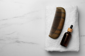 Wooden hair comb, bottle of essential oil and terry towel on white marble table, top view. Space for text