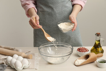 Woman putting flour into bowl at white wooden table, closeup