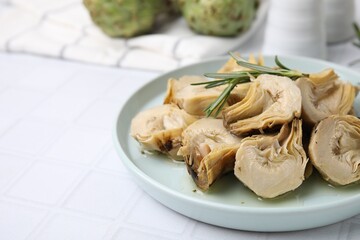 Plate with pickled artichokes and rosemary on white tiled table, closeup