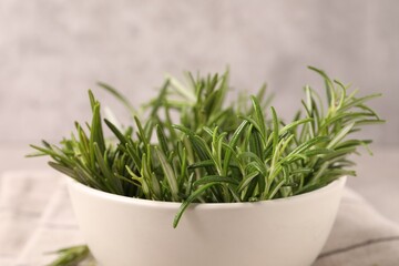 Bowl with fresh green rosemary against blurred background, closeup