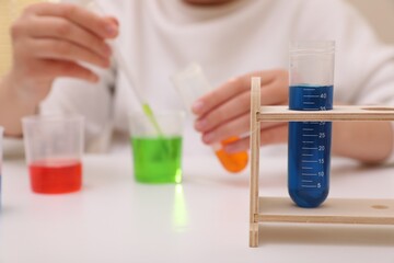 Girl mixing colorful liquids at white table indoors, selective focus. Kids chemical experiment set