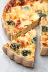 Delicious homemade quiche with salmon and broccoli on light gray table