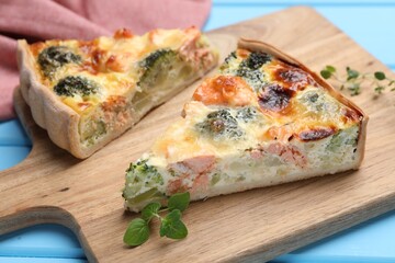 Delicious homemade quiche with salmon and broccoli on wooden board, closeup