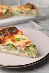 Piece of delicious homemade quiche with salmon and broccoli on light grey table, closeup