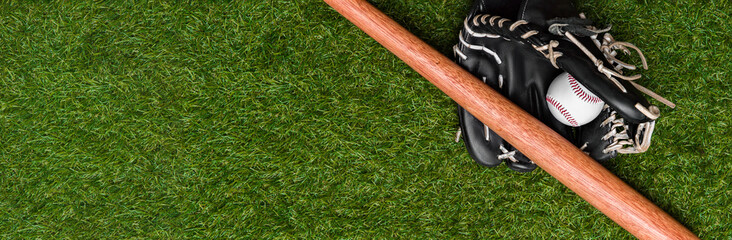 Baseball bat, glove and ball on green grass field. Sport theme background with copy space for text and advertisment