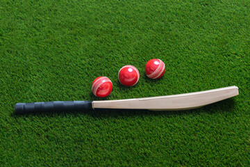 Cricket bat and red ball on green grass background. Horizontal sport theme poster, greeting cards,...