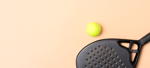 Black professional paddle tennis racket and ball with on beige background. Horizontal sport theme...