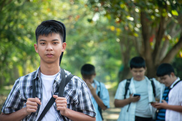 Portrait of young asian boy with black guitar back on his back, standing in front of his friends during the way to back home, soft and selective focus, concept for young teenager lifestyle.