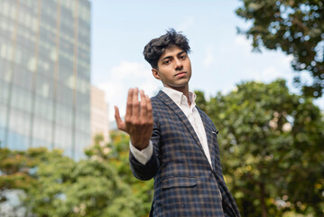 A stylish guy in a blue checkered suit in a serious face calling with a hand gesture while standing...