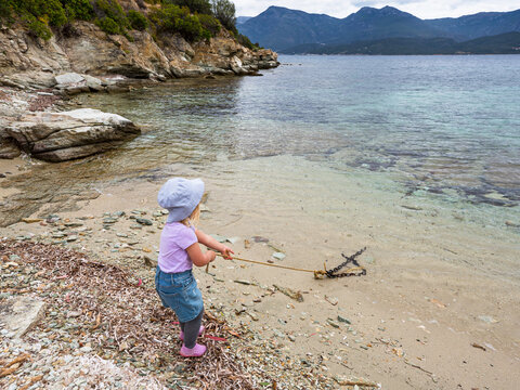 Little girl pulling boat anchor outside transparent turquoise water at the small creek near Corsica Saint Florent city. France