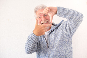 Obraz premium Portrait of happy bearded senior man in blue casual sweater gesturing photo frame looking at camera smiling standing on white background