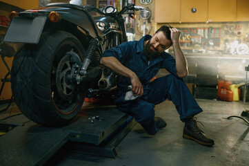 Fototapeta na wymiar Satisfied smiling mechanic feeling glad looking at repaired motorcycle
