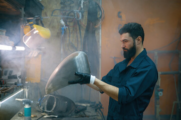 Serious concentrated repairman inspecting new welded part for motorcycle
