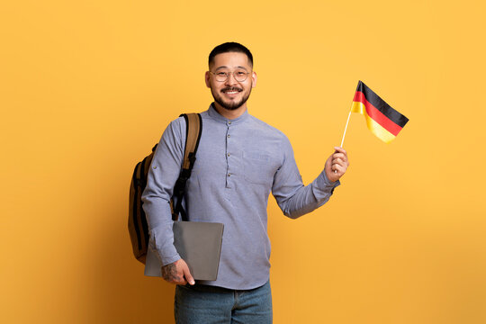 Online Language Courses. Smiling Young Asian Man Holding German Flag And Laptop