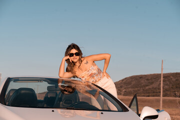 The young girl poses in a white car during summer vacation.