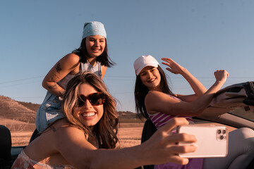 During the summer trip the young girl takes a selfie while her friends smile and have fun. They are...