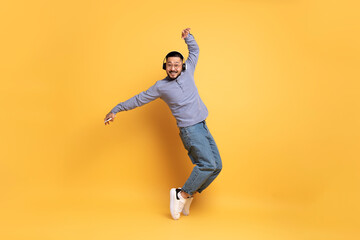 Fototapeta na wymiar Cheerful Asian Man Wearing Wireless Headphones Dancing Over Yellow Background