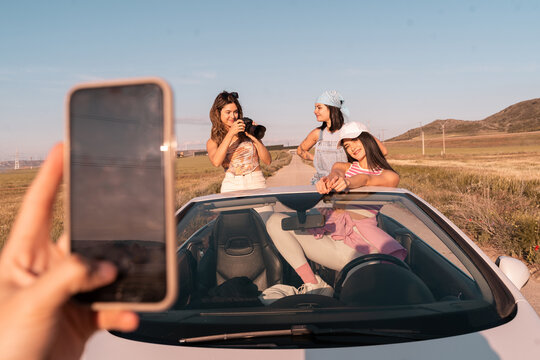 The three friends are on the road during a summer road trip. A friend takes a picture of them with his mobile phone.
