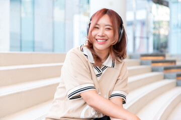 happy female asian student listen music with wireless headphone and smartphone with technology education in campus college library after class and exam for relax in high school or university