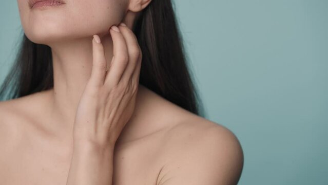 The seminude woman runs her well groomed hand over her chin and down to her neck. Close up of the perfect chin and slender neck of a woman on a blue background. Slow motion.