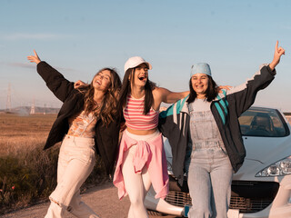 the three beautiful European friends are dancing and hugging on a road and are going to start their summer vacation-