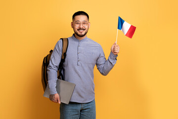Study Abroad. Asian Man With Backpack Holding Laptop And Flag Of France
