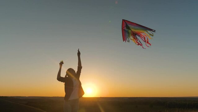 Happy girl plays with kite in her hands on field in rays of sunset. Healthy child dreams of freedom, flight. Girl raises toy airplane into sky, plays outdoors in park. Teenager wants to be pilot. Fly
