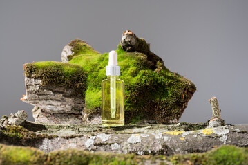 Botella de aceite esencial con cuentagotas sobre un tronco de árbol con musgo	